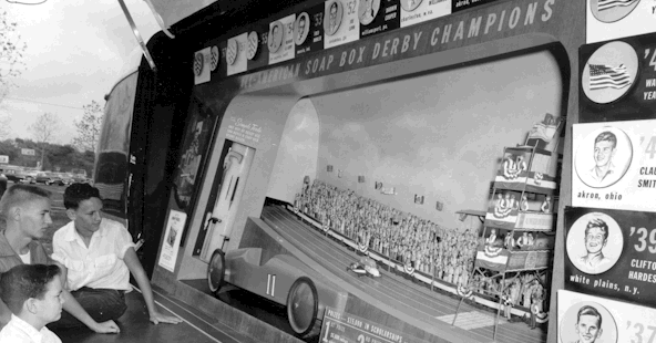 Black and white photo of boys looking at the soap box derby display inside the Futurliner
